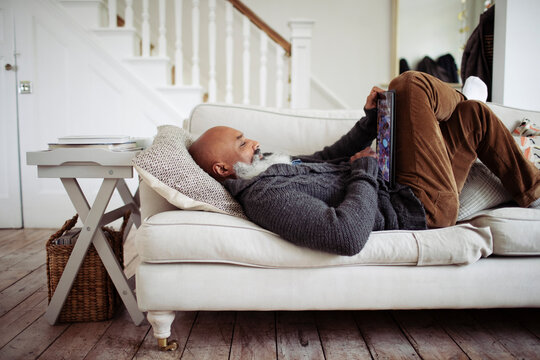 Mature man relaxing on living room sofa with digital tablet