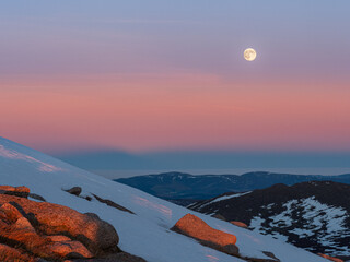 Cairngorms at sunset with colorful Belt of Venus and the rising moon in the sky during the winter season viewed from slopes of Carn Gorm