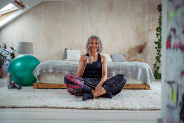 Portrait happy senior woman drinking water on bedroom floor
