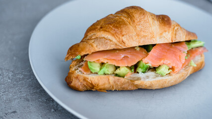Fresh croissant with salmon and avocado. Healthy and tasty breakfast. Healthy diet. Close-up.