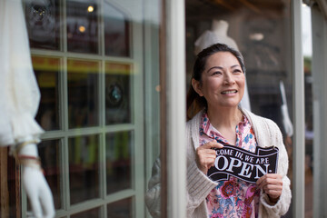 Confident female shop owner holding open sign outside boutique