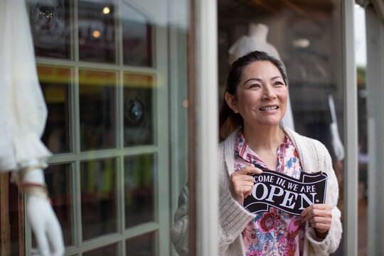 Confident female shop owner holding open sign outside boutique