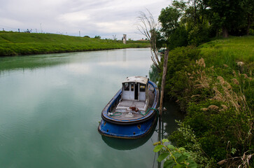 Obraz premium Una barca per la navigazione fluviale ormeggiata a una banchina del fiume Piave lungo la Via Postumia, cammino che parte da Aquileia e arriva a Genova