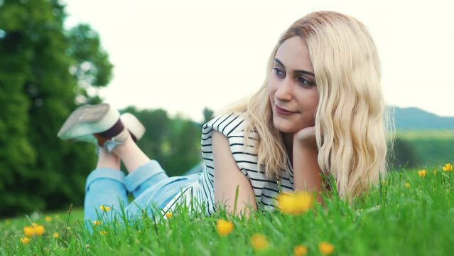 blonde European girl lying on the grass and looking beside. outdoor full shot. High quality 4k footage