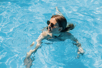happy beautiful woman in sunglasses relaxing in pool water. happy woman in a swimsuit floating in the water