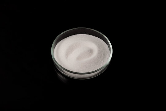 Sodium chlorate. White crystalline powder in a petri dish on a dark background. Chemical inorganic compound. Hygroscopic, readily soluble in water