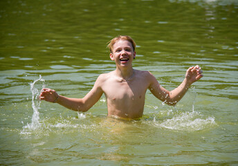 teenager having fun in water of forest lake in summer sunny day with splash