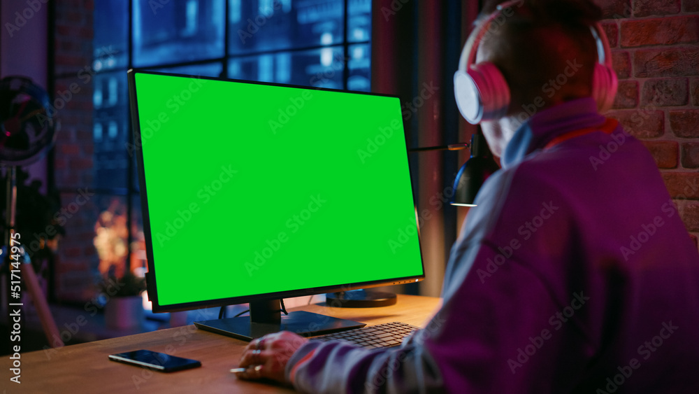 Poster young handsome man in headphones working from home on desktop computer with green screen mock up dis