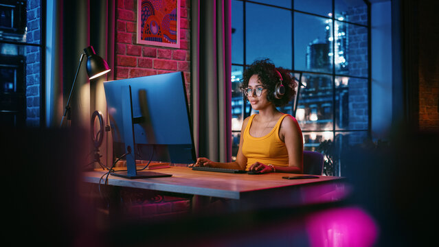 Young Multiethnic Woman In Chatting On Video Call On Computer In Stylish Loft Apartment In The Evening. Happy Creative Female Working From Home, Talking To Client Support Or Family And Friends.