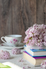 Lilac branches, books and cup of tea or coffee on white wooden table
