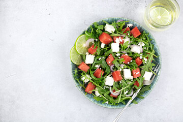 Fresh green salad of arugula, watermelon and feta cheese on a gray background. Top view, copy space.