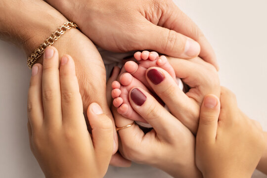 The palms of the parents. A father and mother hold the feet of a newborn child on a white studio background.. The feet of a newborn in the hands of parents. Macro Photography of foot, heels and toes.