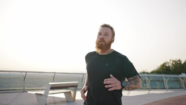 Mature bearded man enjoys jogging on red track on footbridge