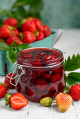 Strawberry jam with whole berries on a white wooden table. Selective focus. 