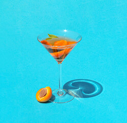 Minimal concept with cocktail glass and a slice of apricot on sunny day. Natural layout on blue...