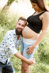 Obraz premium Man with beard draws butterfly on belly of his pregnant girlfriend on a meadow outside in nature