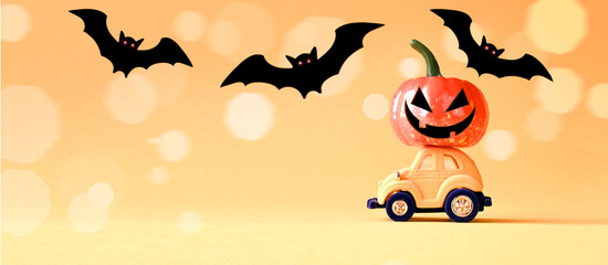Toy car with funny pumpkin on the roof and bats on orange background. Space for text. Halloween...