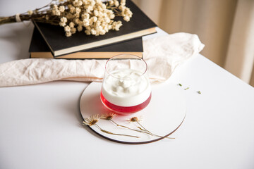 Pause from reading to eat. Pleasant and tasty moment of relaxation and tasting. White table with a glass of strawberry and yogurt gelatin.
