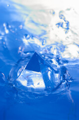 Abstract blue background with water splashen and a geometric object. Pyramid in water.