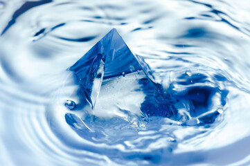 Abstract blue background with water splashen and a geometric object. Pyramid in water.