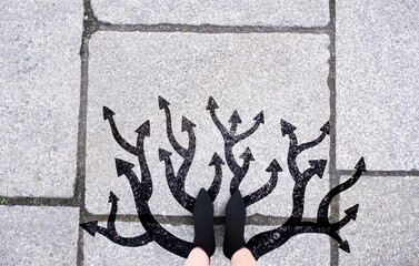 Feet and arrows on road background. Black high heel boots woman on the street walking. Pair of selfie foot standing with many forward arrow direction sign choices.