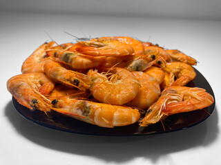 In close-up, there is a black plate on a white table. The plate is full of delicious, cooked and fresh shrimp. A great appetizer with beer. A healthy seafood meal.