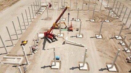 large construction site with precast concrete parts, excavators and a crawler crane building up a hall, aerial view, warehouse, structural engineering, construction