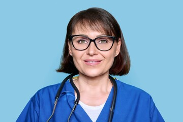 Middle aged female nurse in blue uniform with stethoscope smiling looking at camera