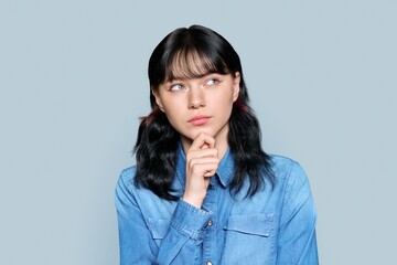 Portrait of pensive young female looking away on gray isolated background