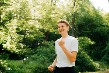 Successful man raises his hands after jogging. Male athlete with raised hands celebrating success and goals after sports exercise and training.