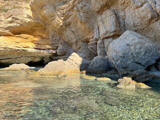 Cave in the sea of island at summer. Pebbles on seabed. Clear calm water surface. Scenic rocks and stones of Mediterranean coast.
