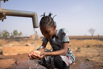 Young African girl happily looking at her handful of water flowing from the village well after a long dry season © Riccardo Niels Mayer