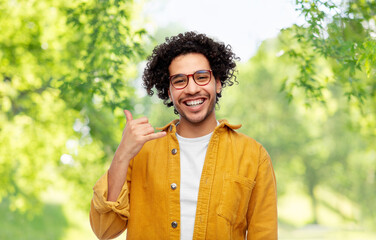 people and fashion concept - happy smiling man in glasses and yellow jacket making phone call gesture over green natural background