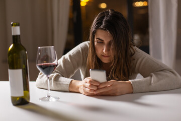 alcoholism, alcohol addiction and people concept - drunk woman or female alcoholic with smartphone drinking red wine at home