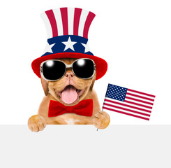 Happy Mastiff puppy wearing like Uncle Sam holds flag USA above empty white banner. isolated on white background