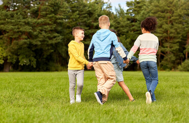 Fototapeta premium childhood, leisure and people concept - group of happy kids playing round dance at park