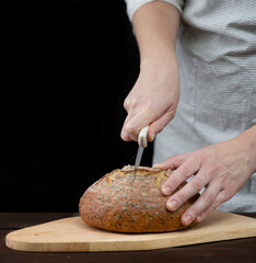 Female hands slicing home-made bread. Isolated on dark background