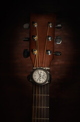 Silver wrist watch on acoustic guitar fretboard neck, shot in studio with a dark wooden background