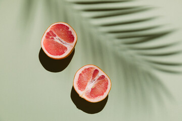 Fresh healthy grapefruit slices on green background with palm leaf shadow. Creative minimal...