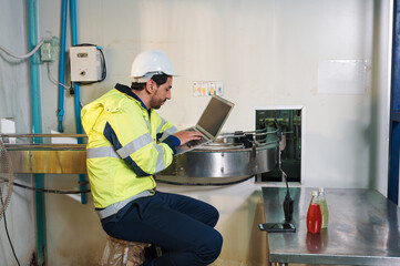 Caucasian engineer man in safety uniform checking and reporting quality a bottled fruit at conveyor belt in processing plant