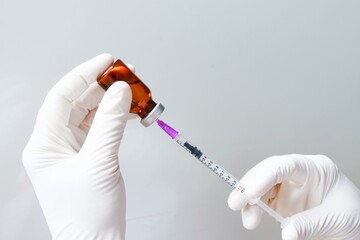 The doctor uses a syringe to suck the vaccine from the bottle. to inject the patient under the...