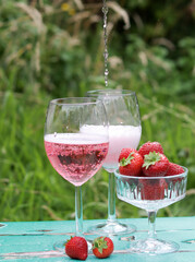 Two glasses of rose sparkling wine and strawberry on a  table. Romantic picnic outdoors. Close up photo of glass tableware. Summer drinks and food. 