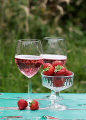 Two glasses of rose sparkling wine and strawberry on a  table. Romantic picnic outdoors. Close up photo of glass tableware. Summer drinks and food. 
