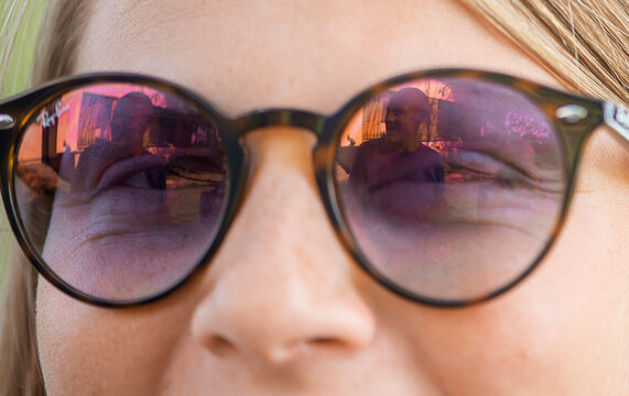 Close-up of a woman's face with sunglasses, reflection of a man in glasses