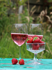 Two glasses of rose sparkling wine and strawberry on a  table. Romantic picnic outdoors. Close up photo of glass tableware. Summer drinks and food. 