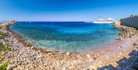 Fototapeta premium Panoramic view of beach, harbor and marina from Saint Paul's Gate of ancient city. Mooring yachts and vessels. Crystal clear turquoise water. A summer vacation in a Rhodes, Dodecanese, Greece.