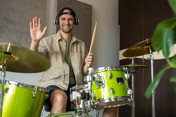 Young man records drum lesson on electronic device in equipped music studio. During lesson man explains concept of playing drums and demonstrates techniques