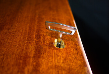 Old metal key in a wooden door on a black background. Mysterious door with an old key close-up