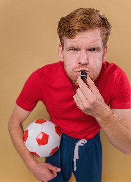 Young funny man football trainer whistle hold soccer ball isolated on beige background studio . People sport humor concept