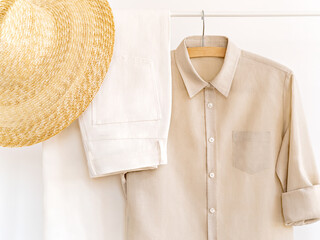 Woman's cotton elegant outfit in shades of beige with straw hat. Rack with summer female clothes on hangers next to wall. Clothing retails concept. Advertise, sale, fashion. Simplicity concept.